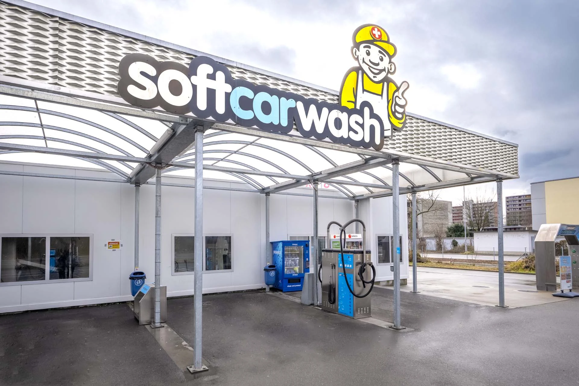 Autolavaggio self-service all'aperto con macchinari blu e un’insegna “Softcarwash” sovrastante.