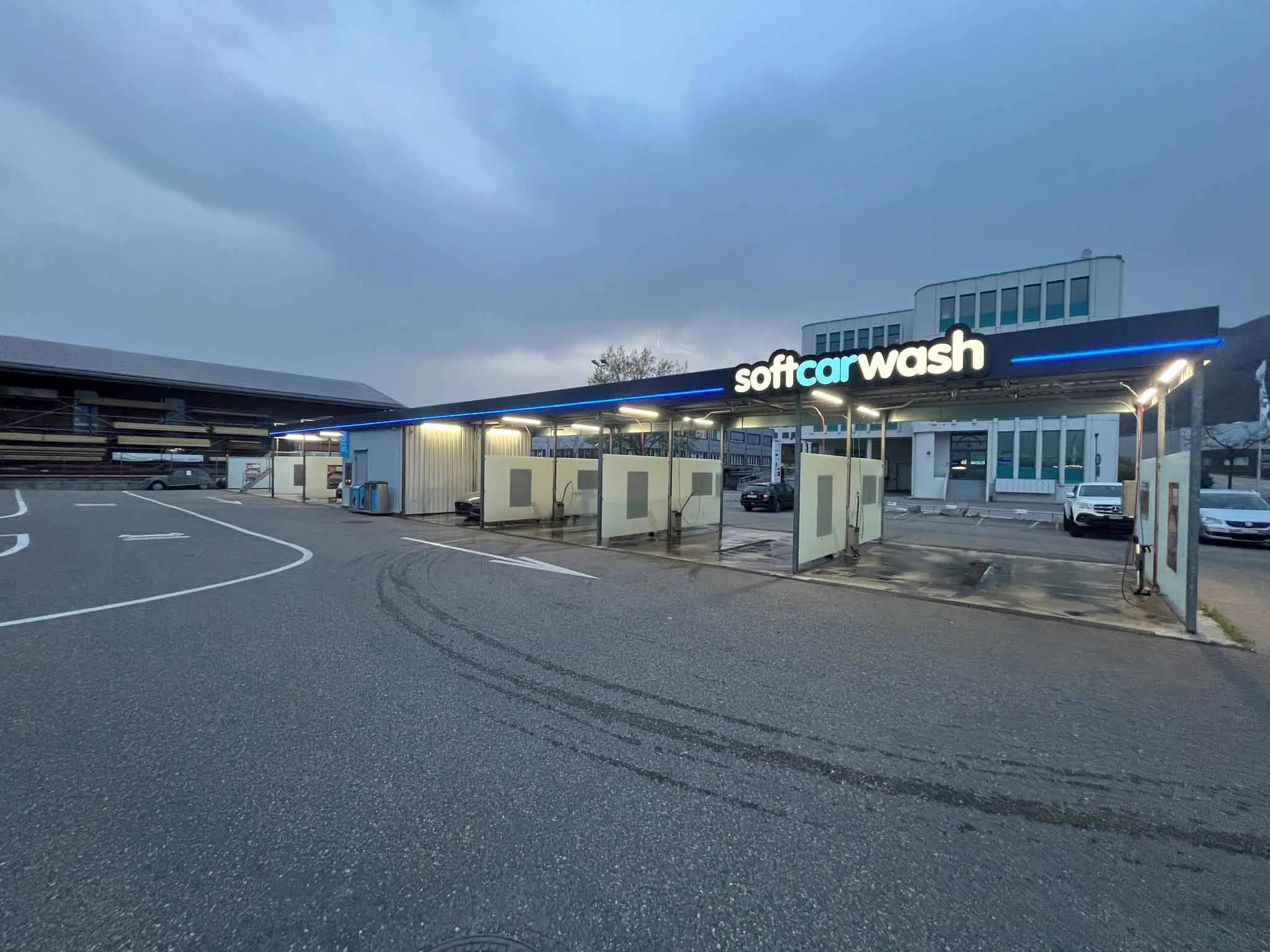 Autolavaggio self-service all’aperto con postazioni di lavaggio, accanto a un edificio, sotto un cielo nuvoloso. Autolavaggio self-service all'aperto con postazioni di lavaggio, accanto a un edificio, sotto un cielo nuvoloso.