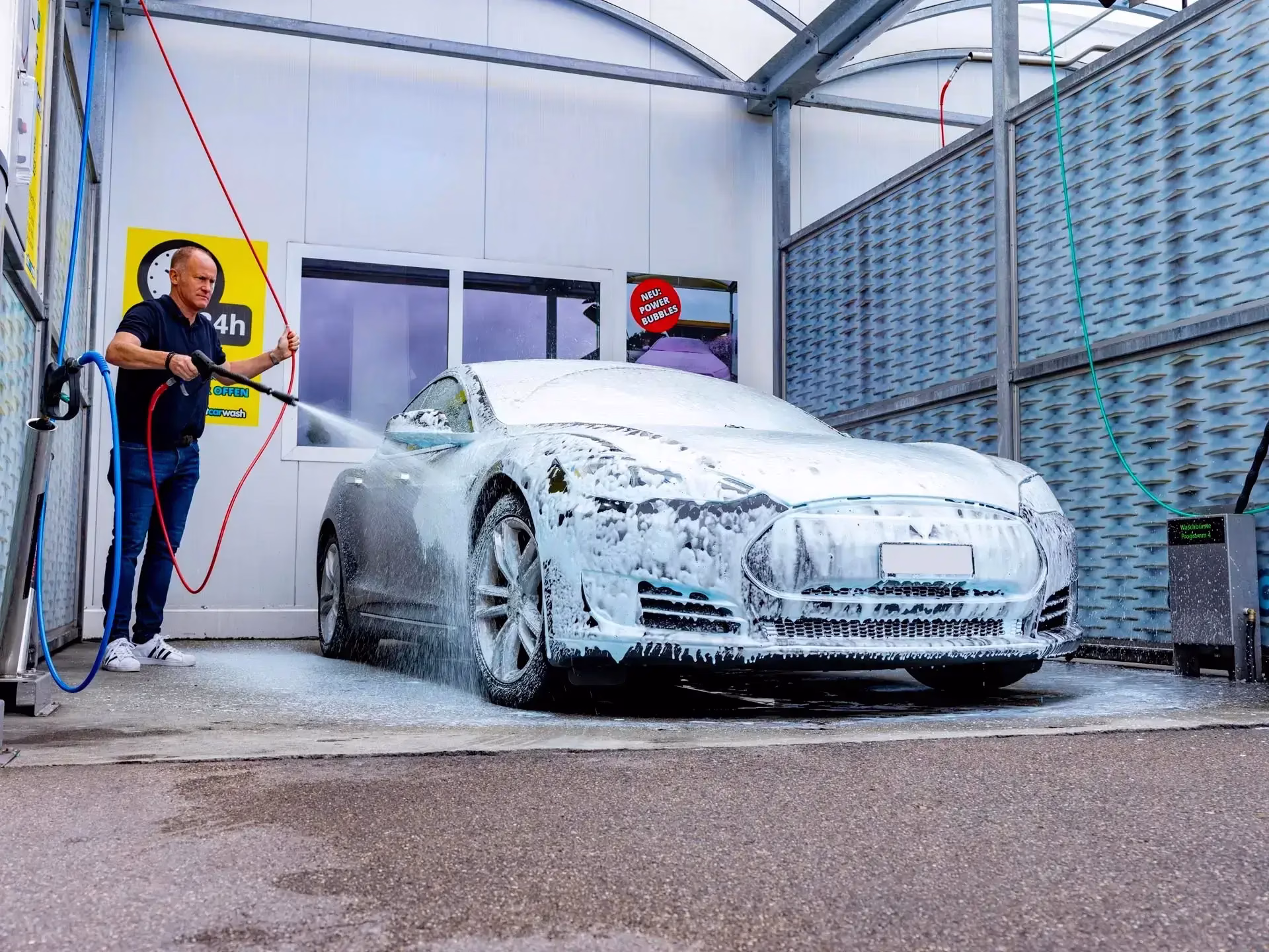 Un uomo che lava un'auto coperta di sapone in un autolavaggio self-service.