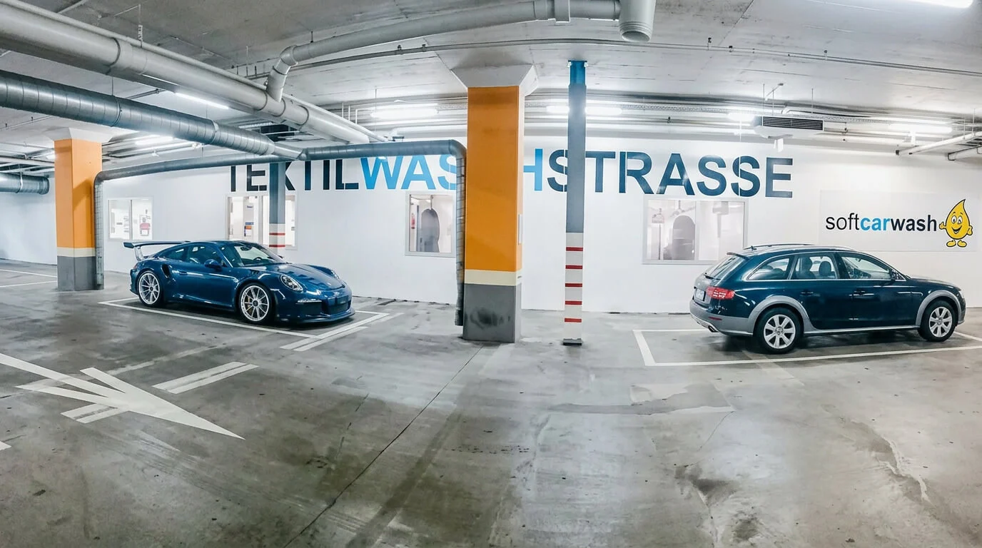 Due auto parcheggiate in un parcheggio sotterraneo vicino a una parete con la scritta “Textilwaschstrasse”. Due auto parcheggiate in un parcheggio sotterraneo vicino a una parete con la scritta “Textilwaschstrasse”.