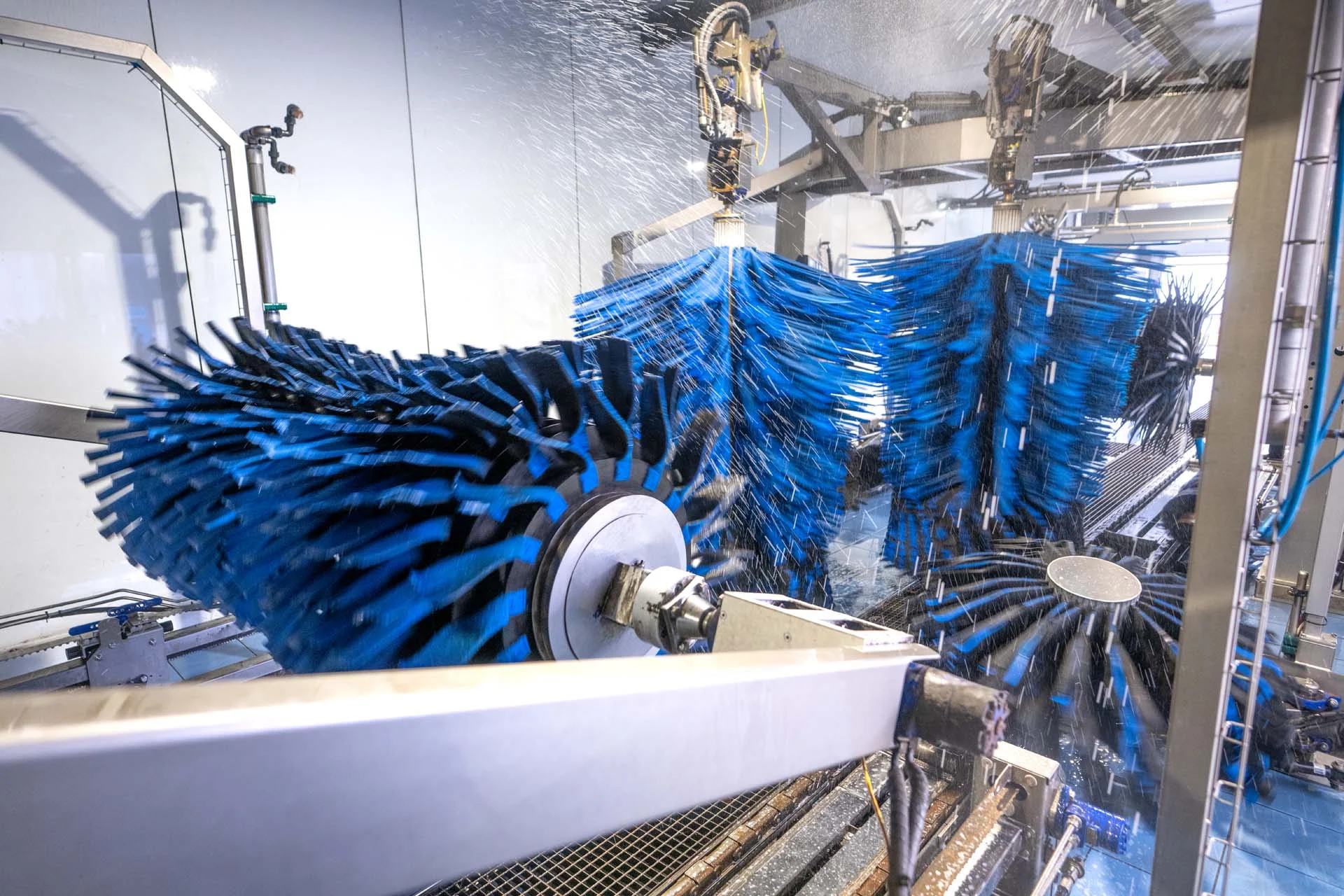 Grandi spazzole rotanti blu che spruzzano acqua all’interno di un impianto di autolavaggio progettato per garantire il massimo comfort.